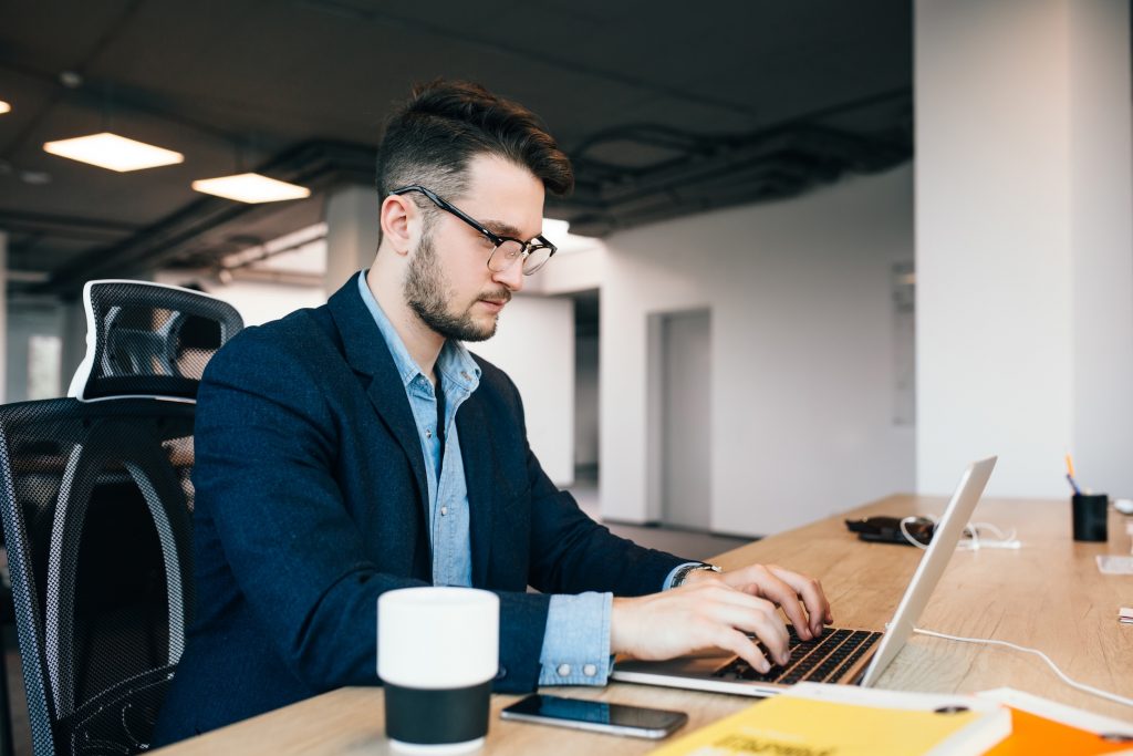 Young dark-haired man is working at the table in office.