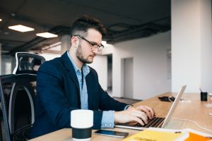Young dark-haired man is working at the table in office.
